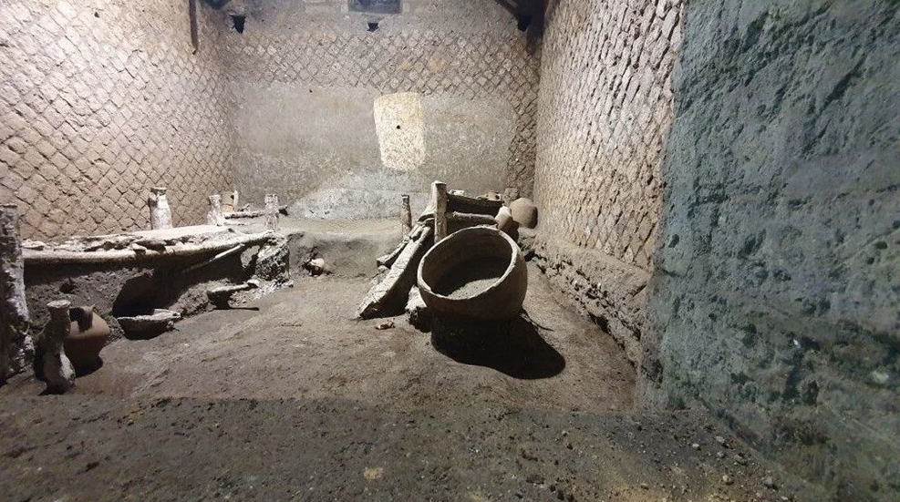 Biri çocuk için olduğu sanılan küçük olmak üzere üç yatak, sekiz amfora, seramik bir çanak ve ahşap bir kutunun kalıntıları keşfedildi. Buluntular, M.S. 79 yılında lavların altında kalan Pompei’de oluşturulan arkeoloji parkının birkaç yüz metre ötesindeki Civita Giuliana semtinde bir villada yapılan kazılarda gün yüzüne çıkarıldı. Aynı yerde bu yılın başında iyi durumda olan bir tören arabası da bulunmuştu. Arkeologlar, bulunan odada muhtemelen tören arabasının günlük bakımıyla uğraşan kölelerin kaldığını tahmin ediyor. Pompei arkeolojik ören yeri Genel Müdürü Gabriel Zuchtriegel, “Bu buluş, neredeyse yalnızca seçkinlere mensup erkekler tarafından yazılan tarihî kaynaklarda nadiren yer alan kölelerin güvencesiz gerçekliğine açılan bir pencere” oldu dedi. Yazılı bir basın açıklaması yapan Zuchtriegel, “Antik toplumun en zayıf katmanlarının nasıl yaşadığına dair bu ‘eşsiz tanıklık’ kesinlikle bir arkeolog olarak hayatımın en heyecan verici keşiflerinden biri oldu” diye ekledi. 16 metrekarelik oda, bir yatak odası ile bir sandık odası ya da depo olarak kullanıldığı düşülen bir oda arasında yer alıyor. Ahşap kutuda da metal ve kumaştan bazı objeler ele geçirildi. Bunların, tören arabasının atlarının koşum takımına ait parçalar olduğu sanılıyor. Yataklardan birinin üzerinde de tören arabasının dingili bulundu. Tören arabası, bu yılın başında bir ahırın sundurmasının altında bulunmuş, 2018’de ahırda da üç atın kalıntıları keşfedilmişti. Yazılı açıklamada, “Olağanüstü şekilde iyi korunan bu oda, kölelerin günlük yaşamına ilişkin gerçeklere nadir bir bakış sunuyor” dendi. Yataklar, yatanın boyuna göre ayarlanabilecek şekilde kabaca birkaç tabaka kalastan oluşuyor. Yatakların perdeli ayakları ise örtülerle kaplı iplerden yapılmış. Yatakların uzunluğu 1,70 metre, genişliği de 1,40 metre. Arkeoloji parkı yetkililerine göre, belki de odada üç kişilik bir köle ailesi yaşıyordu. Yatakların altında amforalar ve lazımlık olabilecek şeyler gibi kişisel eşyalar bulundu. Oda, üst tarafta bulunan bir pencereden gelen güneş ışığıyla aydınlatılıyormuş. Odanın duvarlarında hiçbir süsleme izi görülmüyor, rastlanan tek izin de duvara asılan bir fenerden kaldığı sanılıyor. Kazılar, mezar taşı yağmacılarına karşı mücadele programı çerçevesinde, hâlâ keşfedilecek birçok tarihî kalıntının varlığının bilindiği bir bölgede yürütülüyor. Civita Giuliana villası, yıllardır tarihî eser yağmacılarının hedefi haline geldi. Arkeologlar, köle odasındaki arkeolojik hazinelerin bir bölümünün birtakım yağmacılar tarafından çalınmış olabileceğini düşünüyor. (Ajans Bizim)